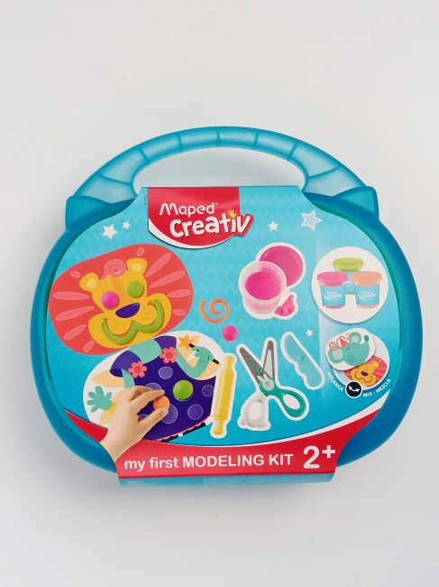 niebieska-walizeczka-z-tekturową-owijką-z-napisem-Maped-Creative-Mój-pierwszy-zestaw-do-modelowania-2+-widać-rysunek-uśmiechniętego-lwa-masy-plastyczne-nożyczki-wałek-plasikowy-nożyk.jpg